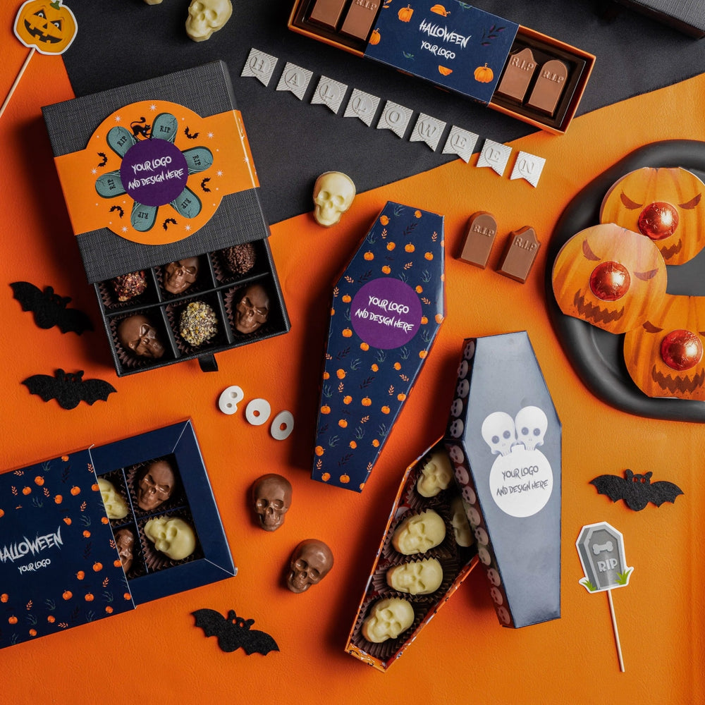 Sfeerbeeld met Halloween chocolade: doosjes met schedelpralines, een doodskist en grafsteenpralines op oranje ondergrond