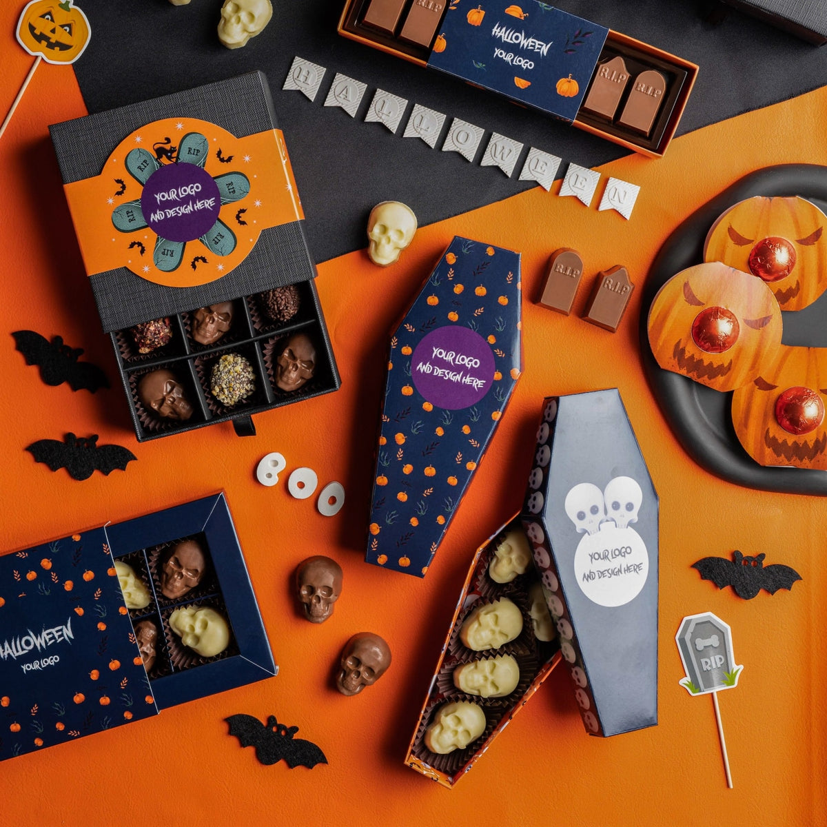 Sfeerbeeld met Halloween chocolade: doosjes met schedelpralines, een doodskist en grafsteenpralines op oranje ondergrond