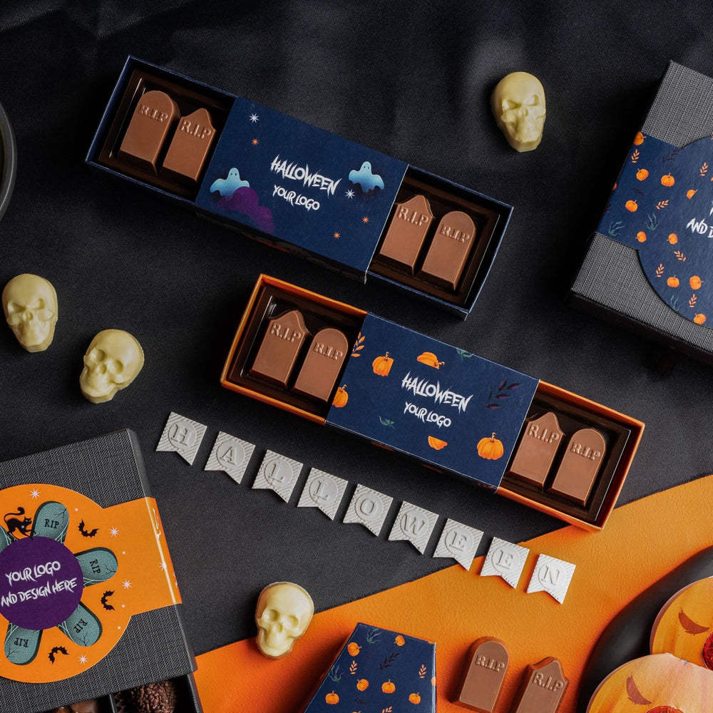 Sfeerbeeld met dozen chocolade grafstenen en losse schedelpralines op een donkere ondergrond