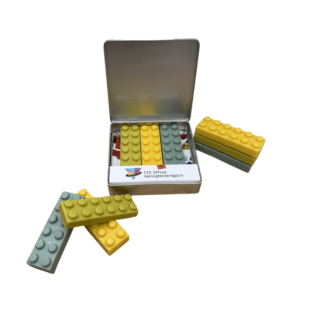 Open plat blik met chocolade bouwstenen in lego-stijl en bedrukte inlay, met losse gele en groene bouwstenen ernaast