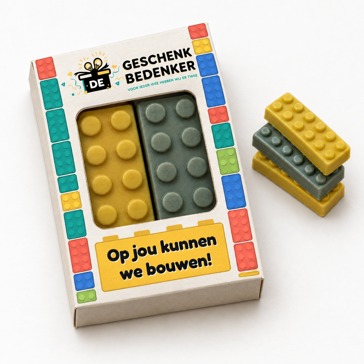 Bedrukt doosje met rechthoekig venster en twee chocolade bouwstenen in lego-stijl, met gestapelde bouwstenen ernaast